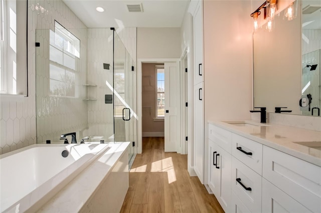 bathroom with plenty of natural light, double vanity, plus walk in shower, and hardwood / wood-style flooring