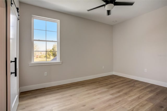 spare room with a barn door, light hardwood / wood-style floors, and ceiling fan