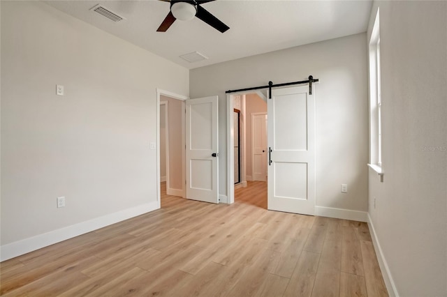 unfurnished bedroom with a barn door, light hardwood / wood-style floors, and ceiling fan