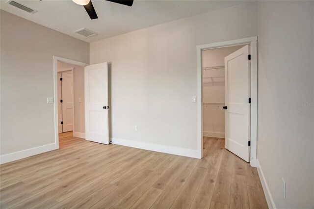 unfurnished bedroom with a walk in closet, a closet, ceiling fan, and light wood-type flooring