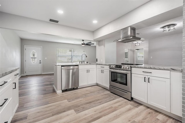 kitchen featuring ceiling fan, island exhaust hood, appliances with stainless steel finishes, light hardwood / wood-style floors, and white cabinetry