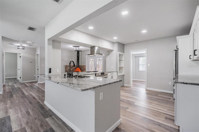 kitchen with exhaust hood, stainless steel range oven, light stone countertops, white cabinetry, and light wood-type flooring