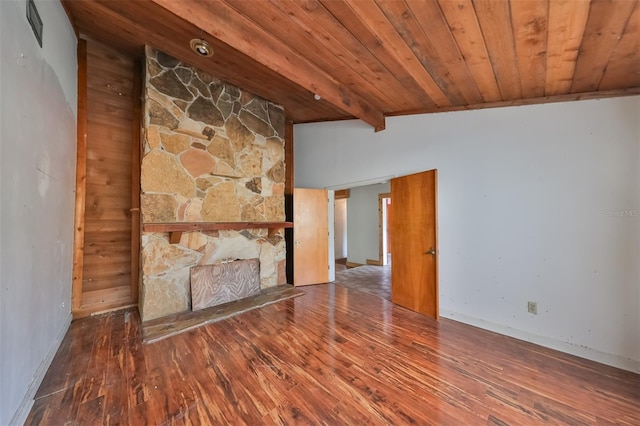 unfurnished living room with vaulted ceiling with beams, wooden walls, a stone fireplace, and dark hardwood / wood-style flooring