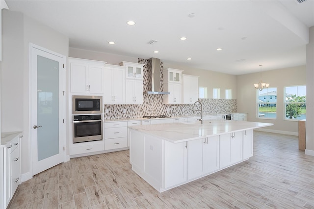 kitchen with white cabinets, a large island, wall chimney range hood, and appliances with stainless steel finishes