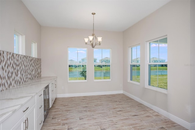 unfurnished dining area featuring a chandelier, a water view, a healthy amount of sunlight, and light wood-type flooring