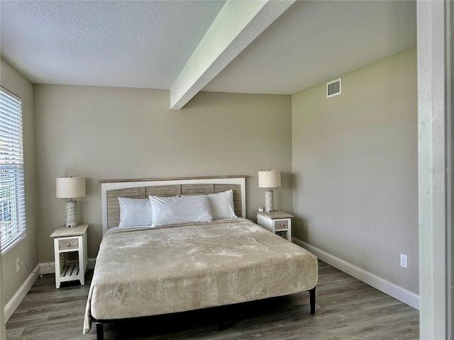 bedroom featuring beam ceiling, dark hardwood / wood-style flooring, a textured ceiling, and multiple windows