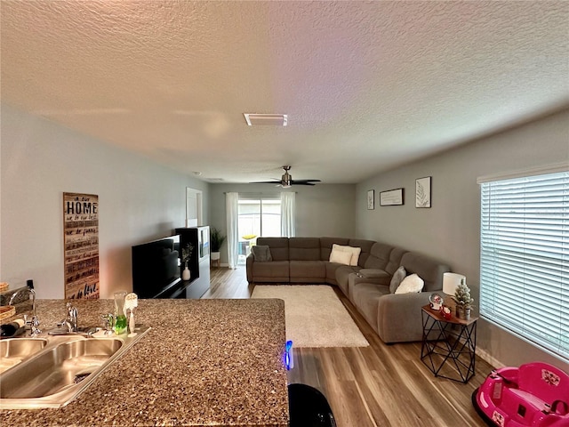 living room featuring visible vents, baseboards, wood finished floors, a textured ceiling, and a ceiling fan