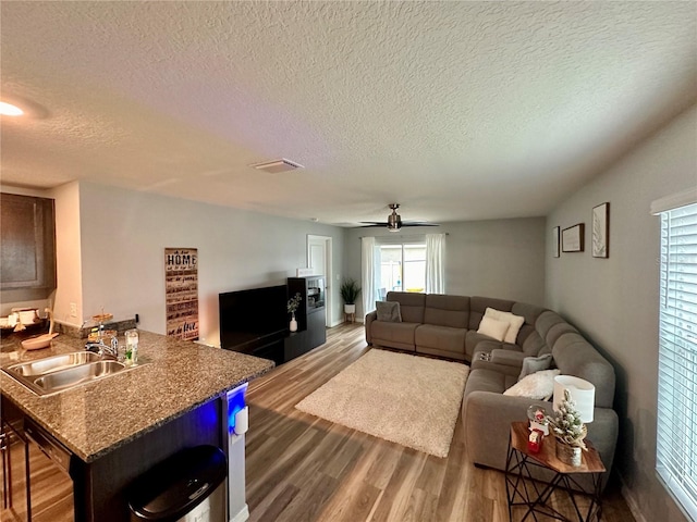 living area featuring a ceiling fan, wood finished floors, visible vents, and a textured ceiling