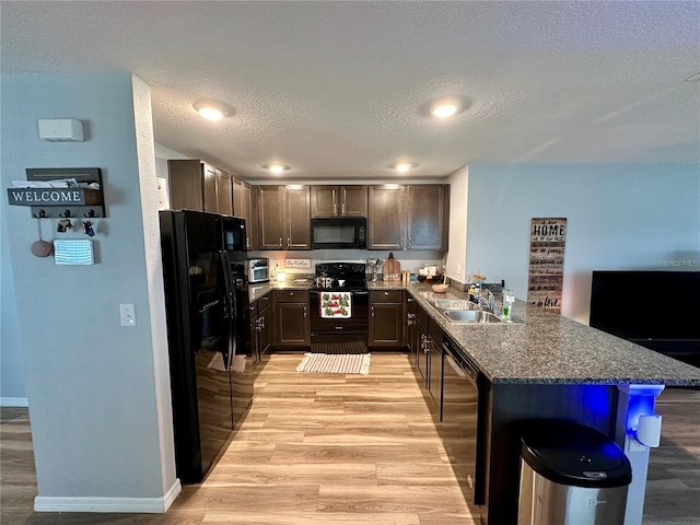 kitchen with a peninsula, a sink, black appliances, dark brown cabinets, and light wood-style floors