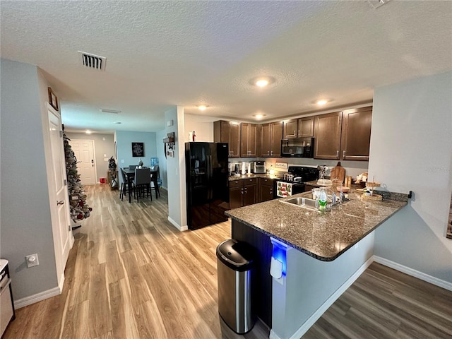 kitchen featuring dark brown cabinets, visible vents, light wood-style floors, and black appliances