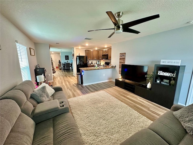 living room with light wood-style flooring, a ceiling fan, visible vents, and a textured ceiling