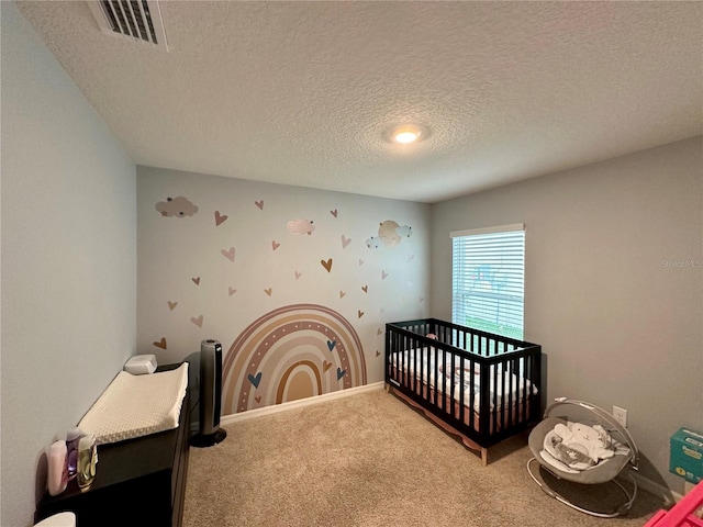 bedroom with a nursery area, visible vents, a textured ceiling, and carpet flooring