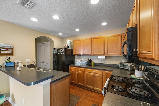 kitchen featuring dark hardwood / wood-style floors, kitchen peninsula, sink, black appliances, and a textured ceiling