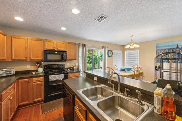 kitchen with decorative light fixtures, dark wood-type flooring, black appliances, a textured ceiling, and a chandelier