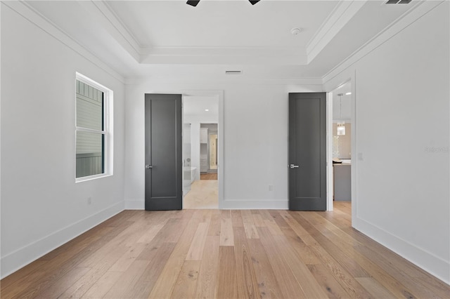 unfurnished bedroom with ceiling fan, a raised ceiling, ornamental molding, and light hardwood / wood-style flooring