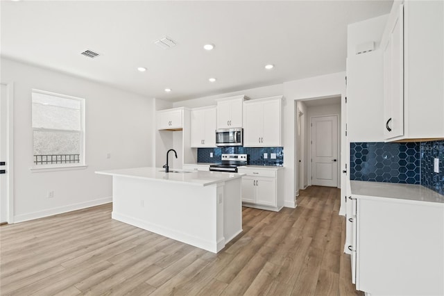 kitchen with white cabinetry, light hardwood / wood-style floors, appliances with stainless steel finishes, and a kitchen island with sink