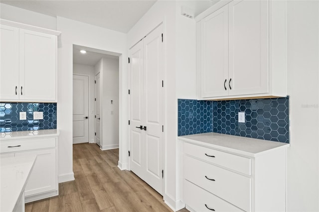 kitchen with light hardwood / wood-style flooring, light stone counters, white cabinets, and tasteful backsplash