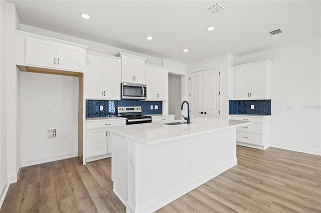 kitchen with white cabinets, a kitchen island with sink, stainless steel appliances, and light wood-type flooring