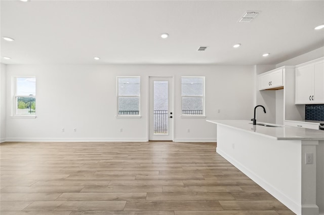 kitchen with white cabinetry, sink, light wood-type flooring, and an island with sink