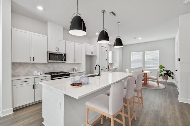 kitchen featuring sink, appliances with stainless steel finishes, a kitchen island with sink, white cabinets, and decorative light fixtures