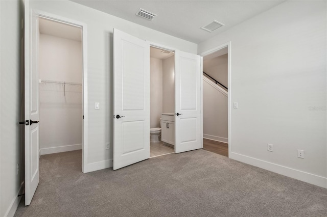 unfurnished bedroom featuring a spacious closet, light colored carpet, and a closet