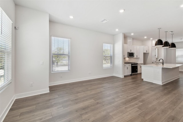 kitchen featuring a center island with sink, pendant lighting, stainless steel appliances, hardwood / wood-style floors, and white cabinets