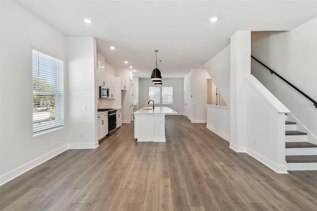 kitchen featuring appliances with stainless steel finishes, a kitchen island with sink, wood-type flooring, white cabinets, and decorative light fixtures