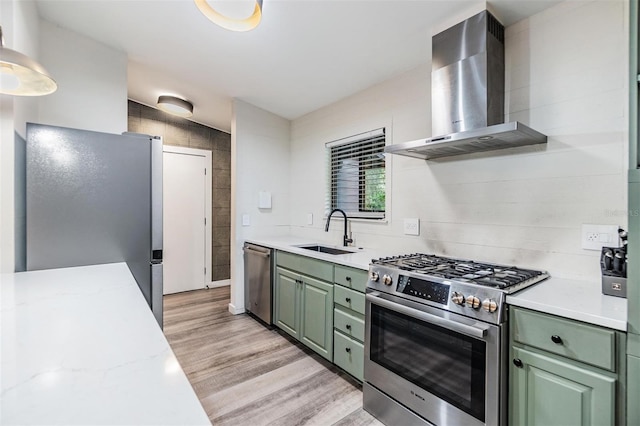 kitchen with stainless steel appliances, sink, light hardwood / wood-style floors, wall chimney exhaust hood, and green cabinets