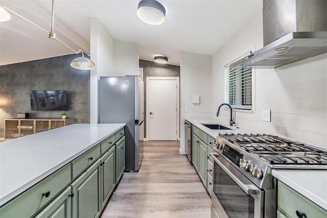 kitchen featuring appliances with stainless steel finishes, sink, light hardwood / wood-style floors, wall chimney exhaust hood, and decorative light fixtures