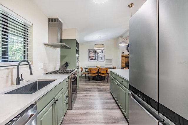 kitchen with wall chimney exhaust hood, stainless steel appliances, sink, decorative light fixtures, and light hardwood / wood-style floors