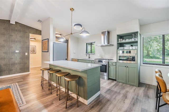 8952 W White Dogwood Dr, Homosassa, FL 34448 - kitchen with green cabinets, appliances with stainless steel finishes, wall chimney range hood, a kitchen bar, and light wood-style flooring