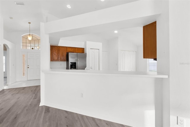 kitchen featuring kitchen peninsula, hanging light fixtures, light hardwood / wood-style floors, vaulted ceiling, and stainless steel refrigerator with ice dispenser