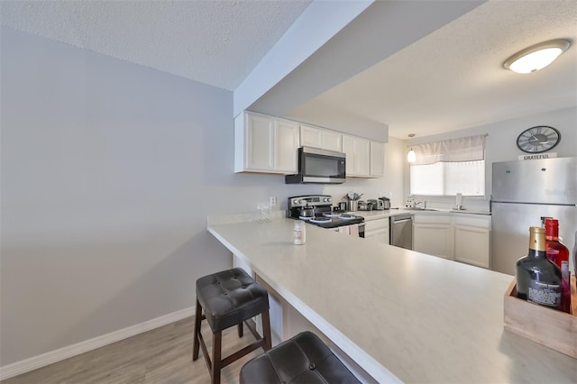 kitchen featuring kitchen peninsula, appliances with stainless steel finishes, light wood-type flooring, white cabinets, and a breakfast bar area