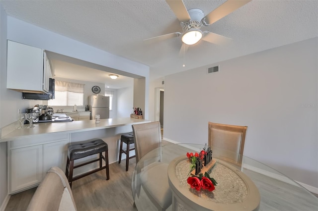 dining area with a textured ceiling, ceiling fan, and light wood-type flooring