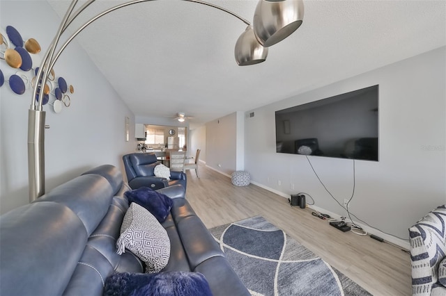 living room with a textured ceiling, ceiling fan, and light wood-type flooring