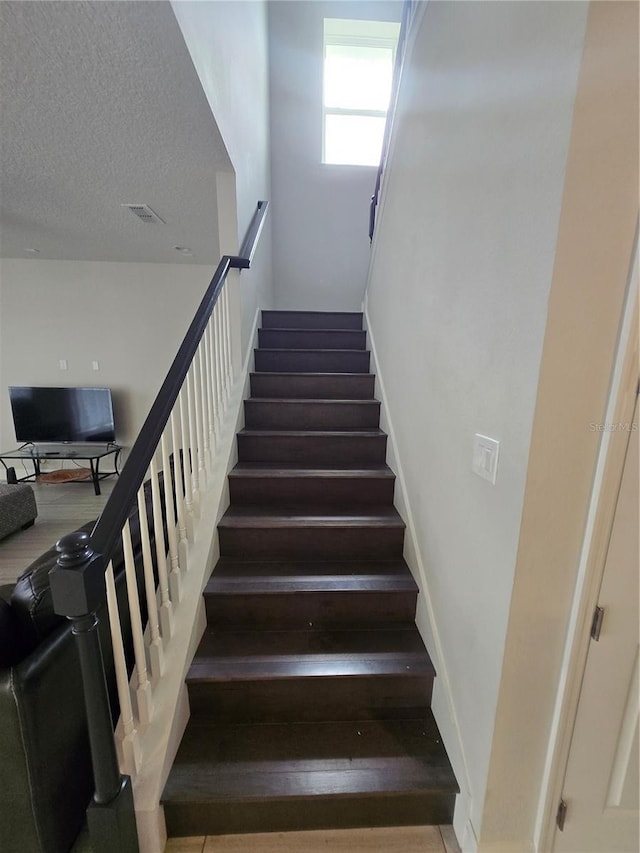 staircase with visible vents and a textured ceiling