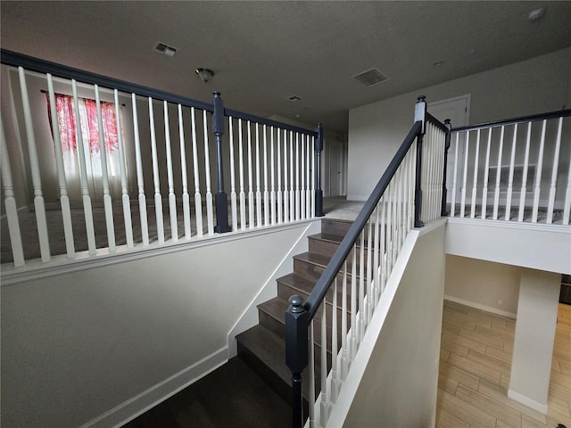 stairway featuring visible vents, baseboards, and wood finished floors