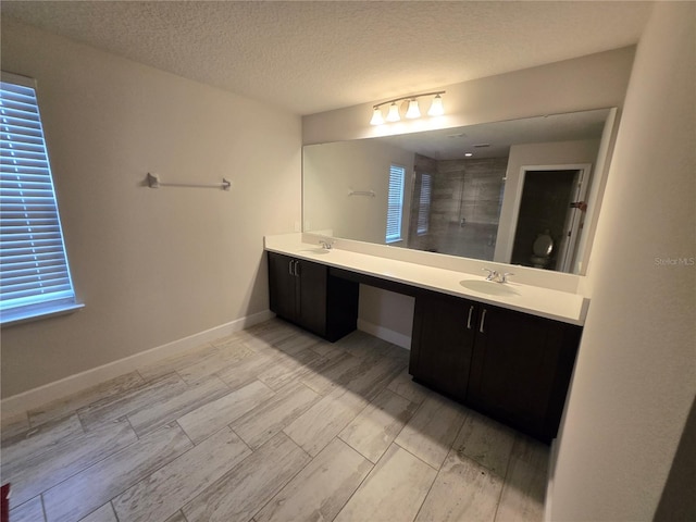 bathroom featuring baseboards, double vanity, a stall shower, a sink, and a textured ceiling