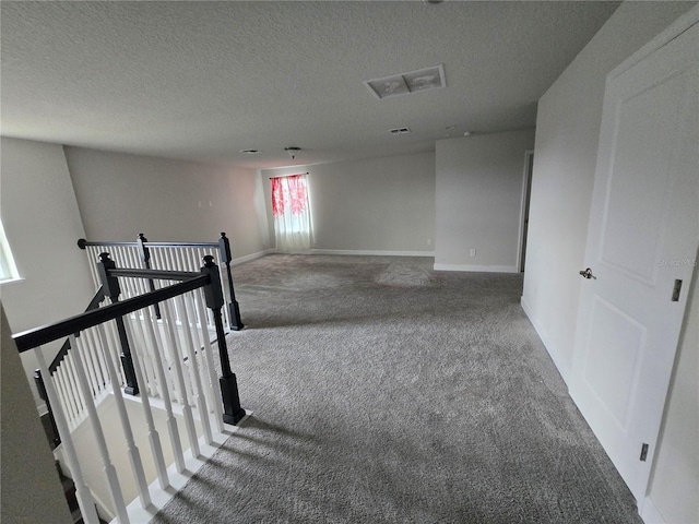 corridor featuring an upstairs landing, a textured ceiling, baseboards, and carpet floors