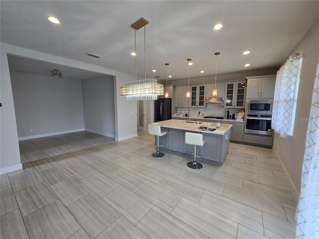 kitchen with tasteful backsplash, light countertops, appliances with stainless steel finishes, a kitchen breakfast bar, and a sink