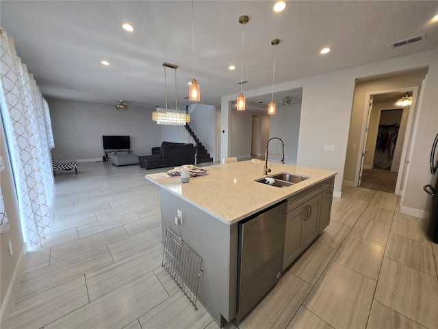 kitchen with visible vents, a sink, a center island with sink, gray cabinets, and stainless steel dishwasher