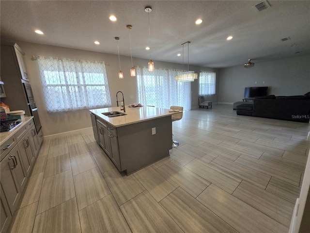 kitchen with a sink, cooktop, light countertops, wall oven, and open floor plan