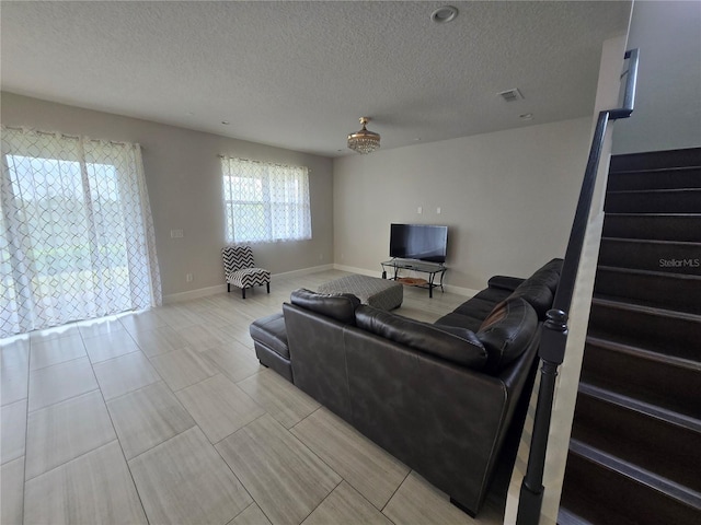 living room featuring baseboards, stairway, a textured ceiling, and visible vents