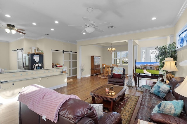 living room featuring a barn door, ornamental molding, ceiling fan with notable chandelier, and light wood-type flooring