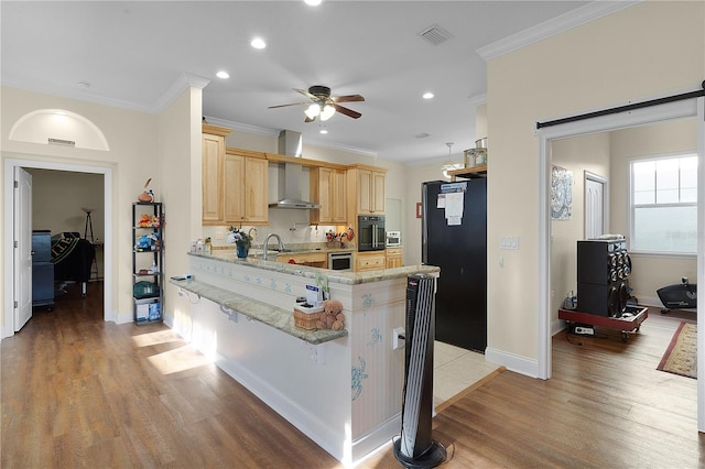 kitchen featuring wall chimney exhaust hood, light hardwood / wood-style floors, ceiling fan, and black appliances