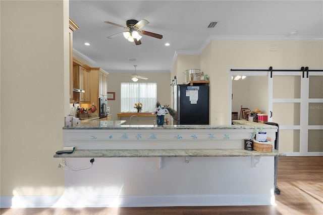 kitchen with light stone counters, ceiling fan, light hardwood / wood-style floors, a barn door, and black fridge