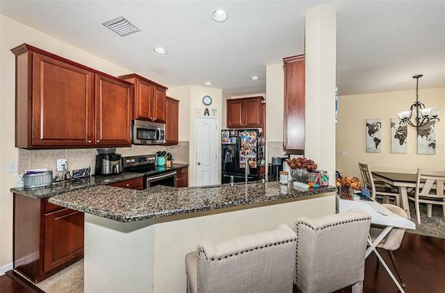 kitchen with appliances with stainless steel finishes, a breakfast bar area, dark stone countertops, and kitchen peninsula