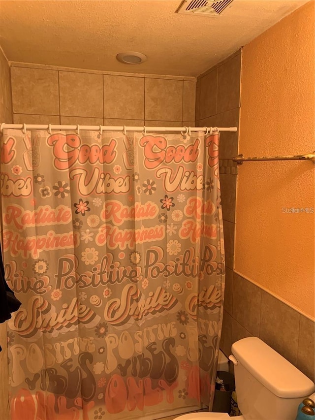 bathroom featuring a textured ceiling, toilet, and tile walls