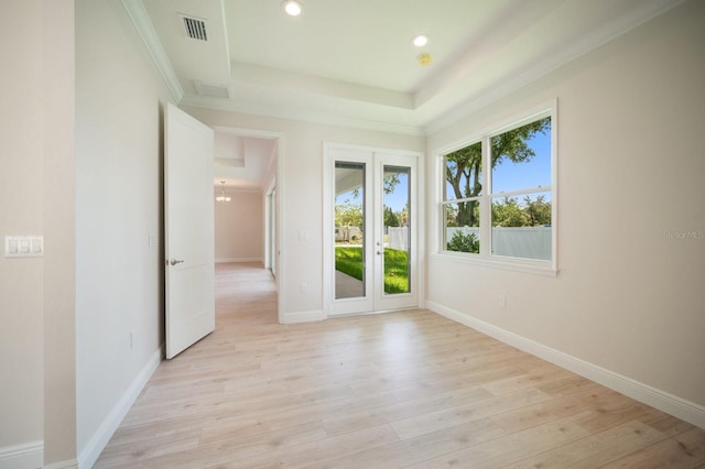 empty room featuring a raised ceiling, light wood-type flooring, and french doors