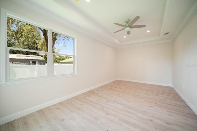 empty room with a raised ceiling, ceiling fan, and light wood-type flooring